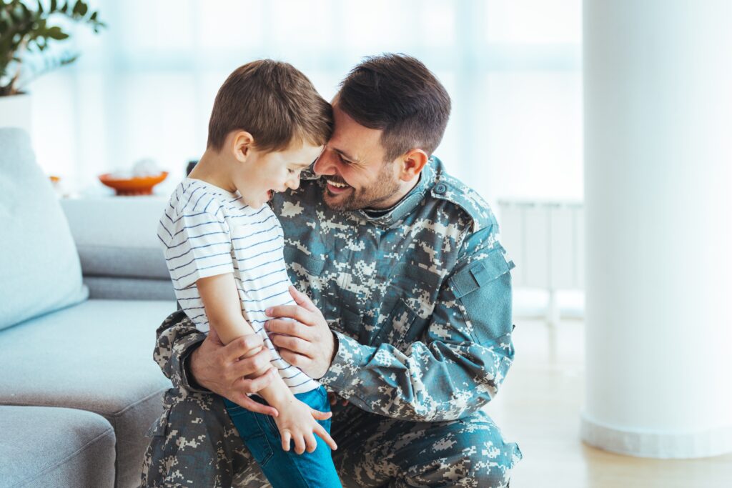 Playful military man having fun with his small son who is smiling at home.